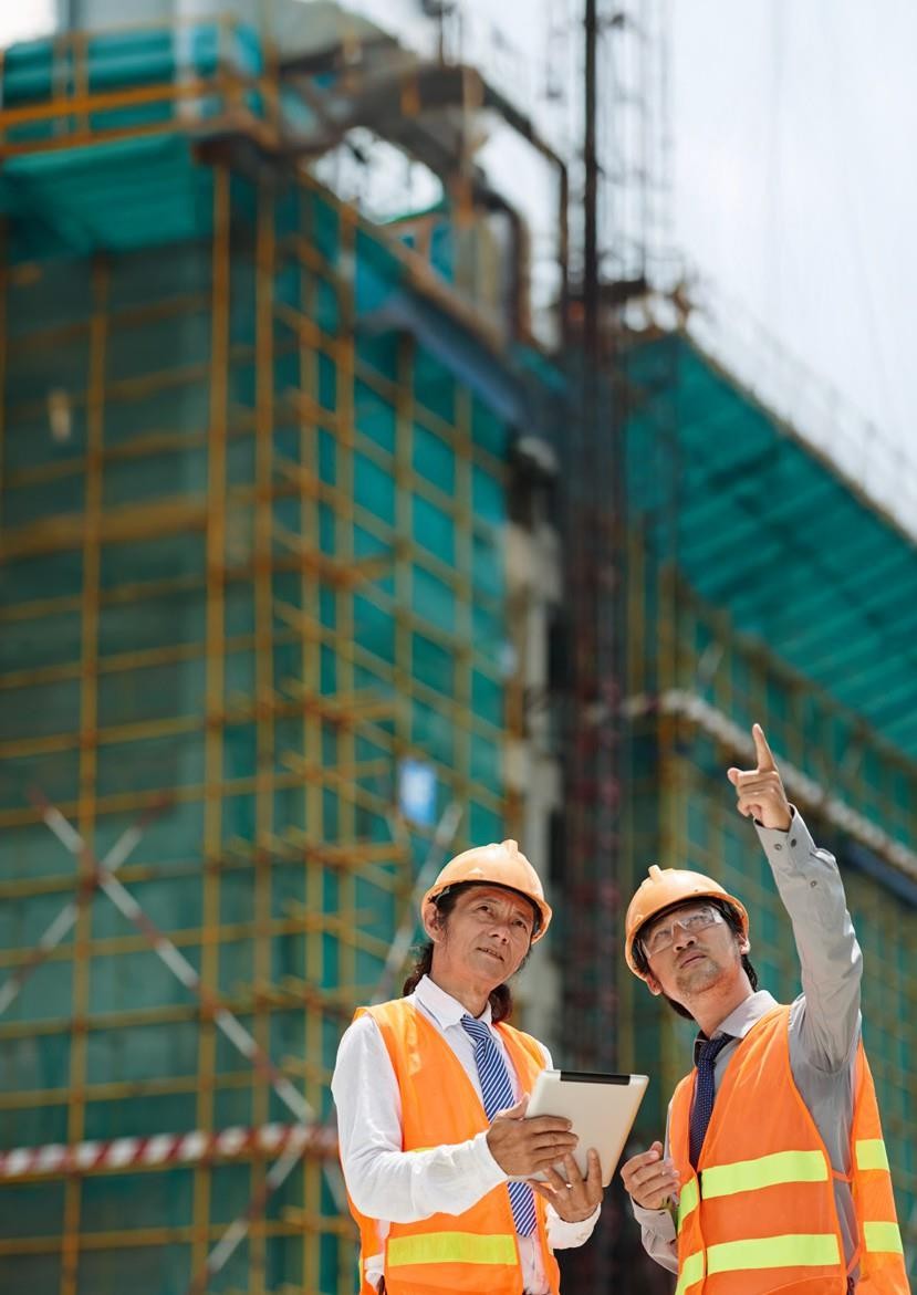 Two engineers in safety vests reviewing a tablet in front of a scaffolded building