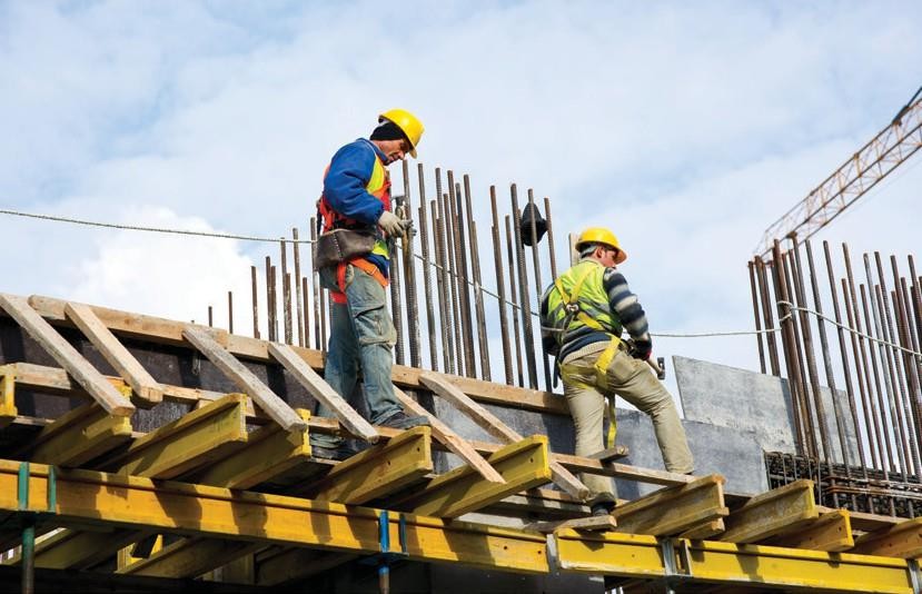 Two workers in hardhats walking across a scaffold beam on a construction site