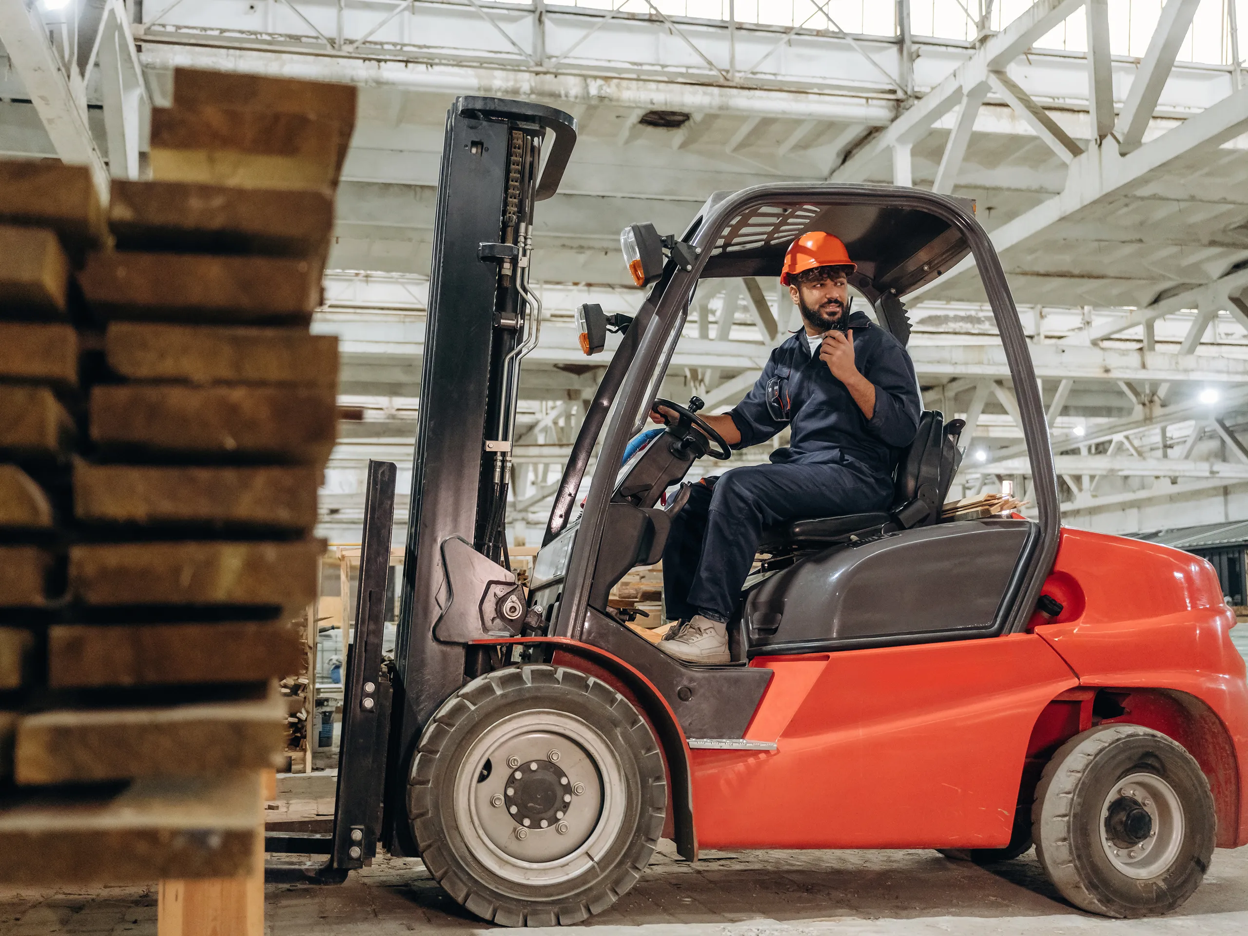 Forklift operator preparing to move a stack of timber in a warehouse